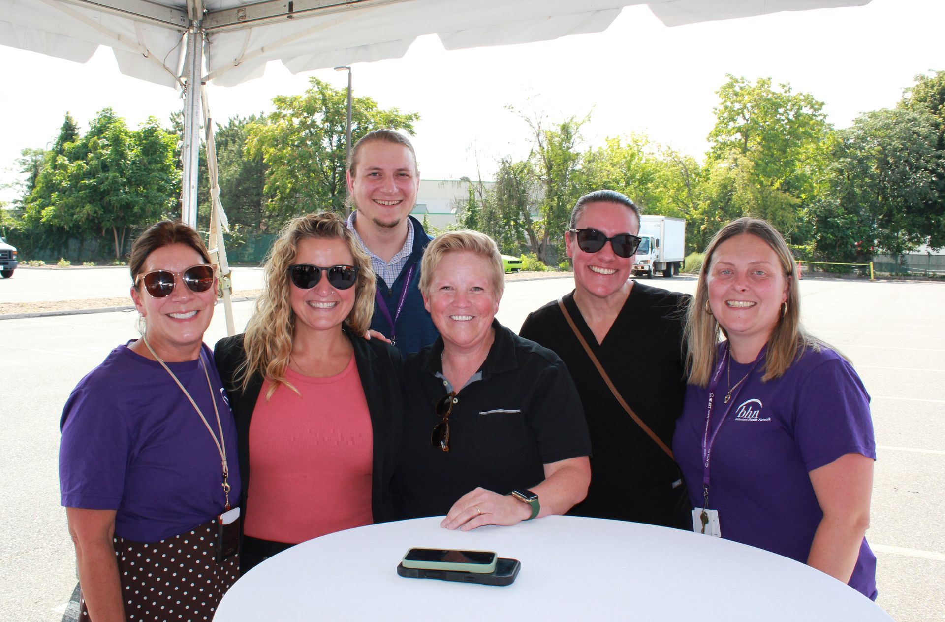 A group of 6 BHN staff members smile for a photo while standing at a table under a tent.