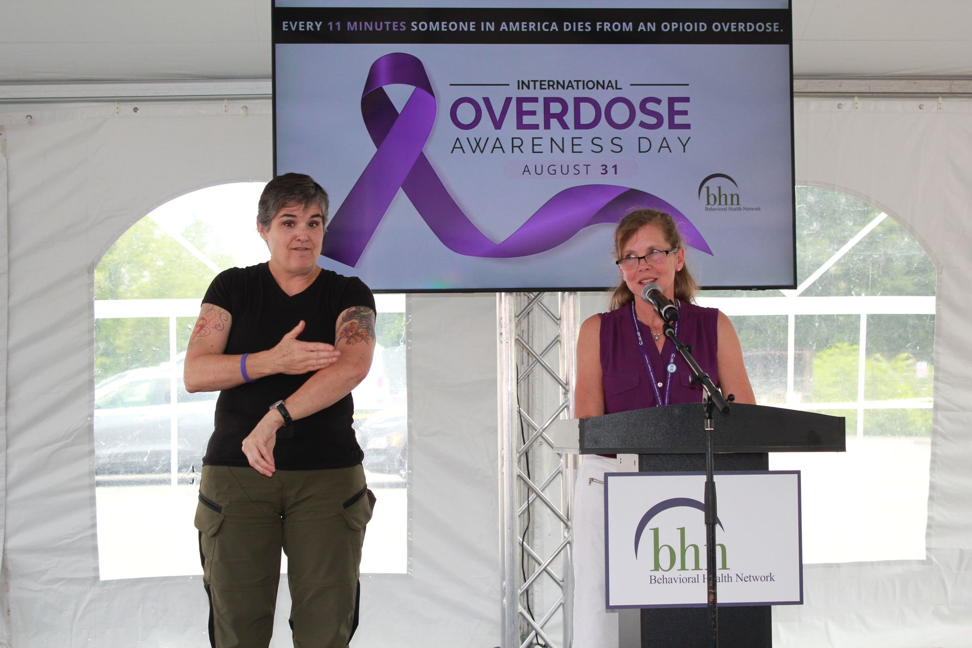 A woman gives a speech at BHN's International Overdose Awareness Day event with a sign language interpreter interpreting her speech next to her.