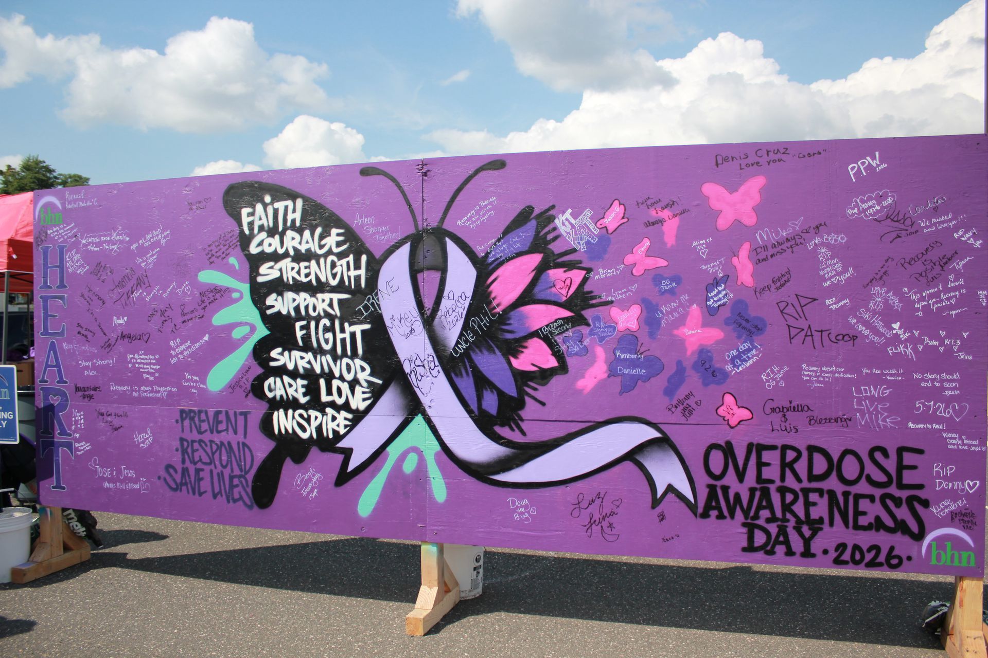 A purple board is decorated with a large purple ribbon in the center and many handwritten messages and positive affirmations for International Overdose Awareness Day.