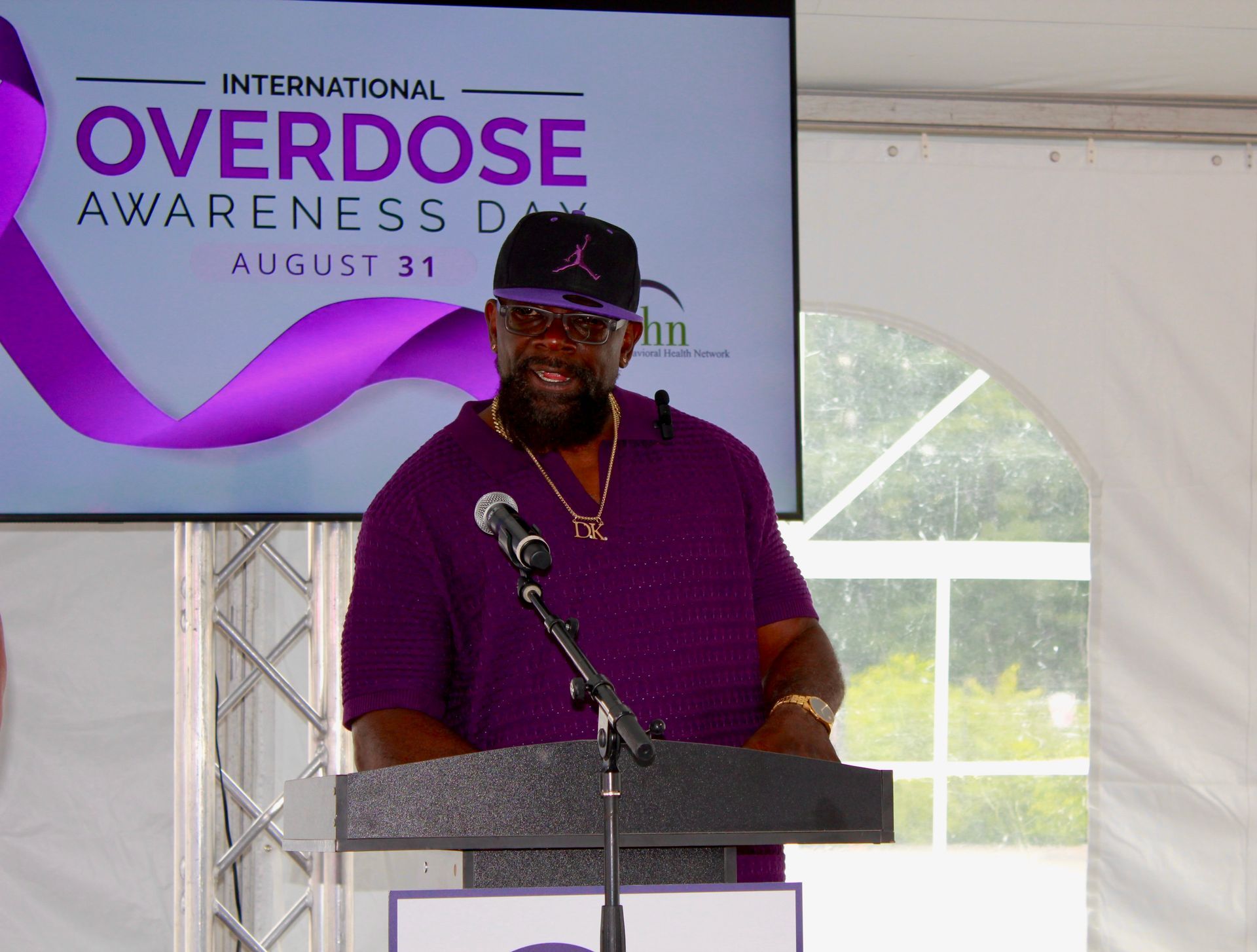 A man wears purple in support of International Overdose Awareness Day while giving a heartfelt speech during BHN's International Overdose Awareness Day event.