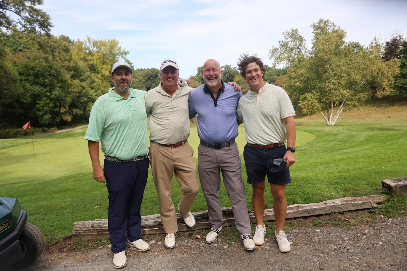 4 men smile and take a group photo on at a golf event on a sunny day.