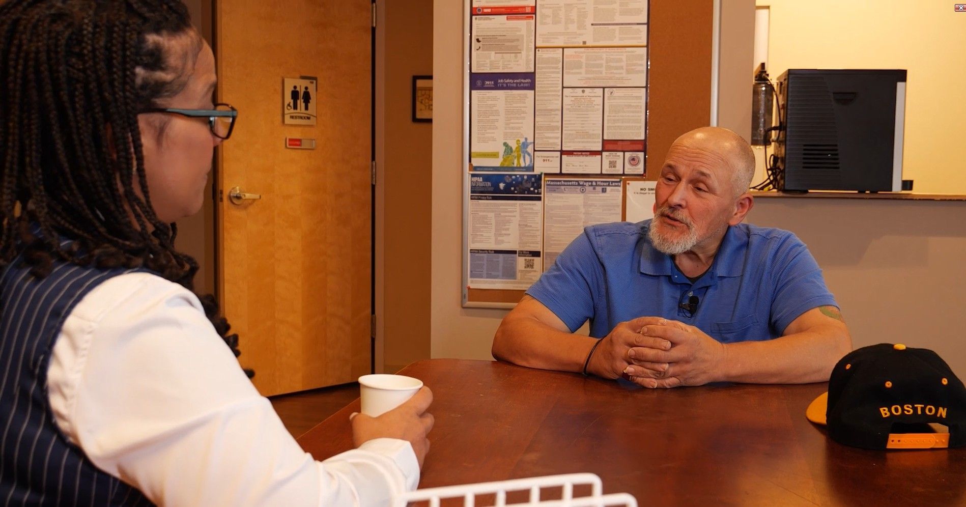 Two people talking across a table in a warm-lit office or meeting room.