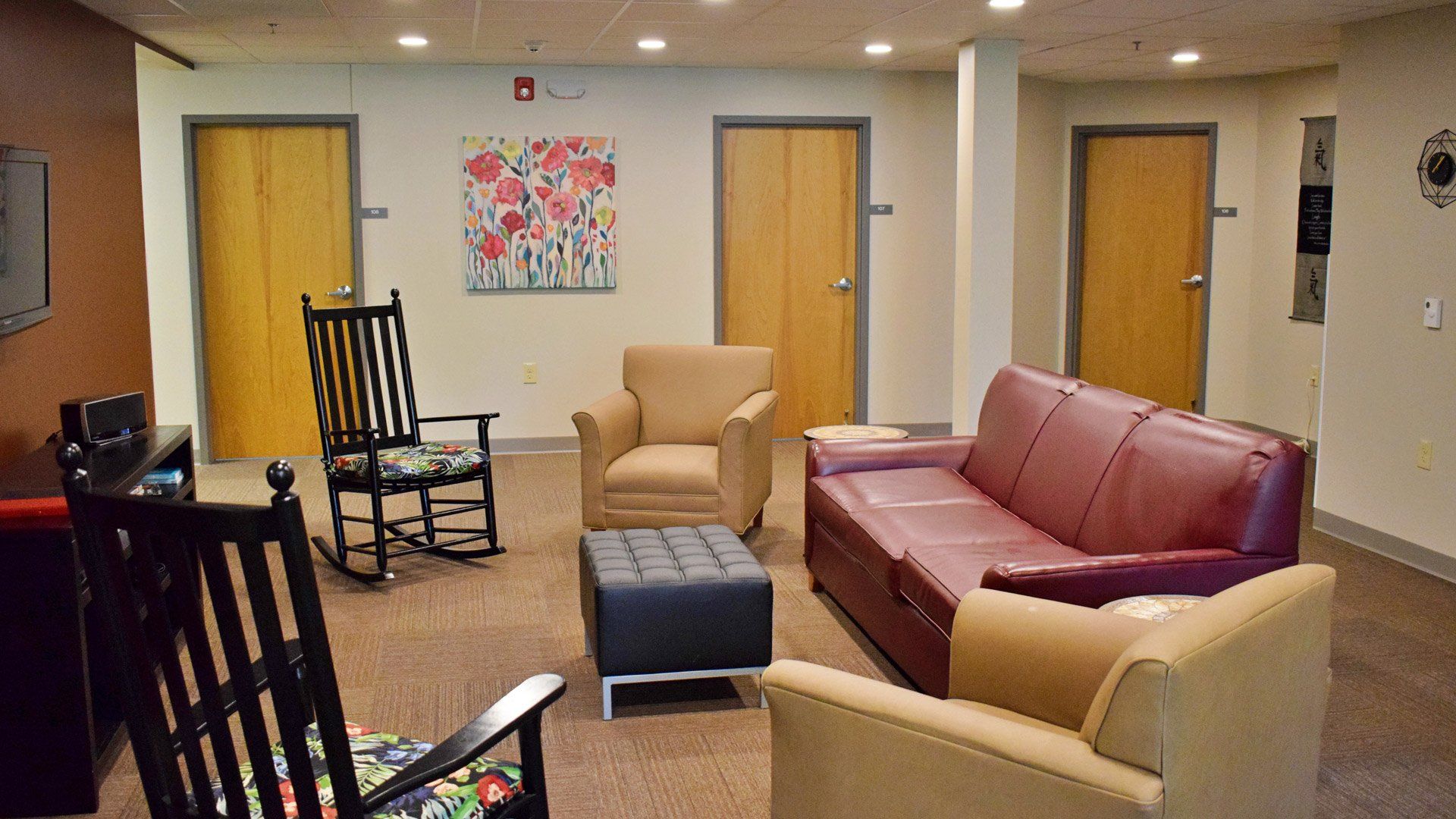 Common room with red sofa, tan armchairs, rocking chair, and doors in the background.
