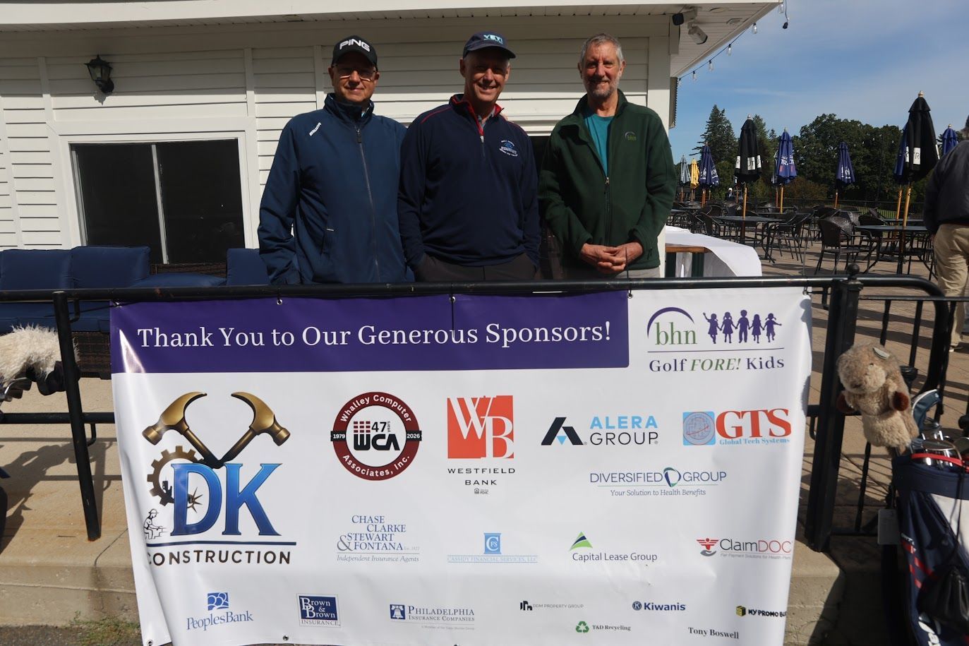 CEO Steve Wynn poses with two men in behind a banner of all the sponsors of BHN's Golf FORE! Kids fundraiser