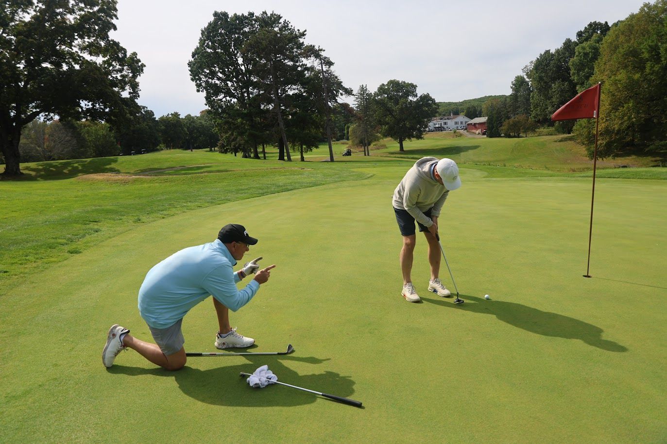 A golfer kneels on the green while pointing at another golfer