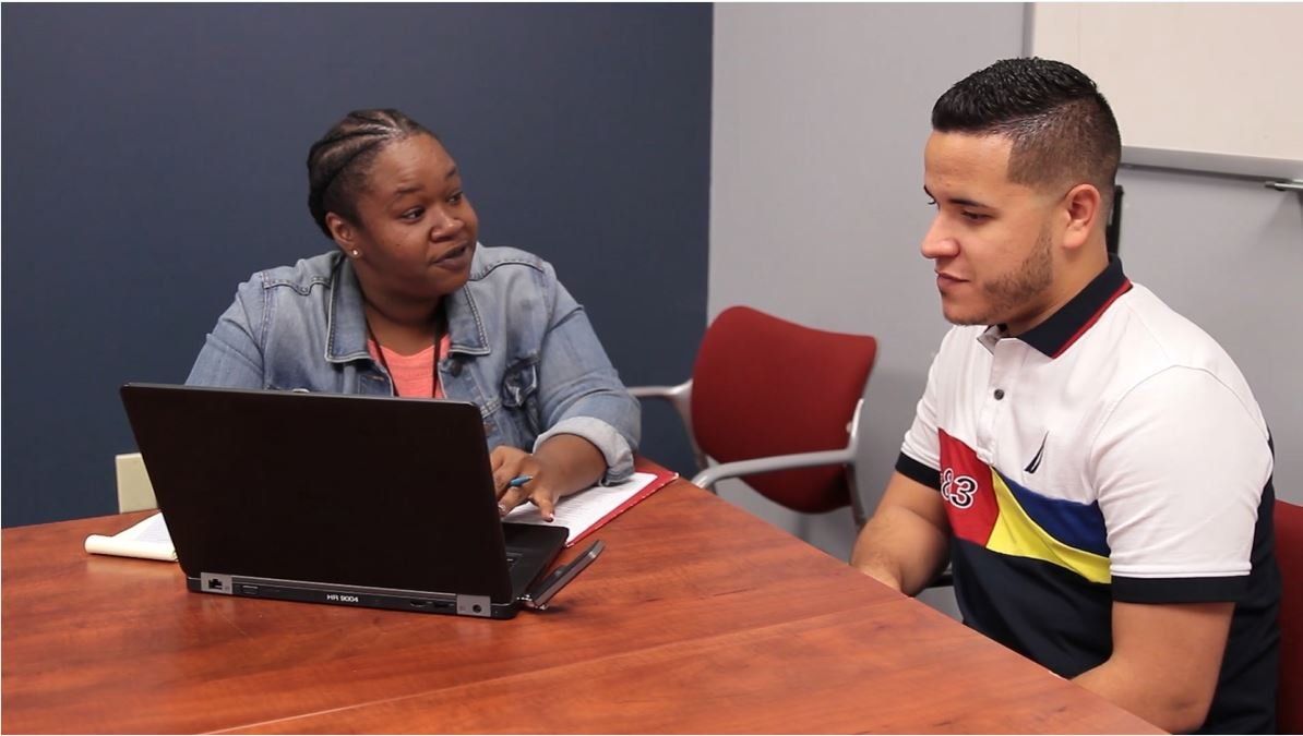 Two people discussing at a table with a laptop in a meeting room