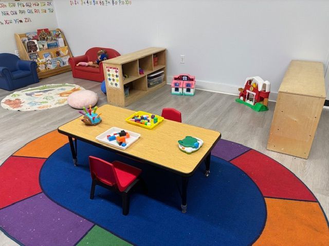 Colorful preschool playroom with a small table, chairs, toys, and a play rug