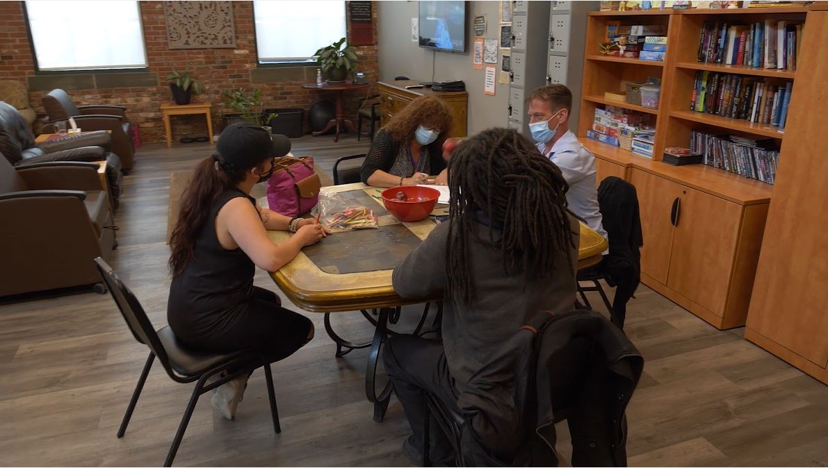 People seated around a table in a cozy room, sharing a game or activity near bookshelves.