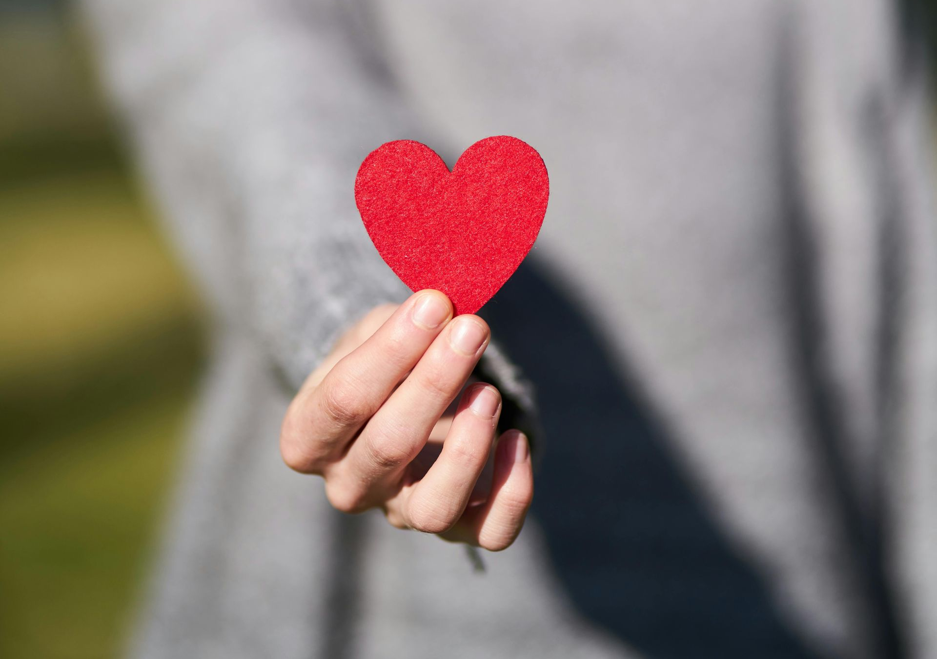 Hand holding a small red felt heart against a blurred gray background
