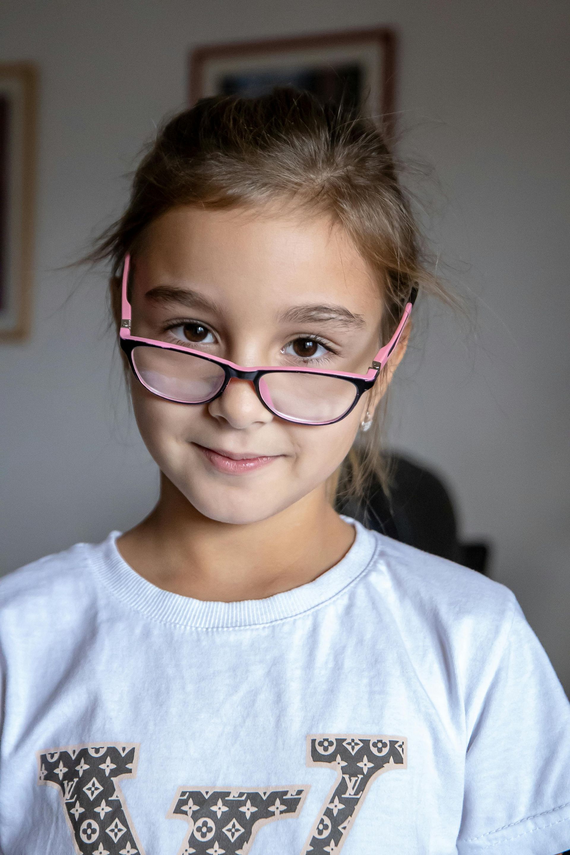 Young person wearing pink glasses and a white shirt, looking at the camera with a slight smile.