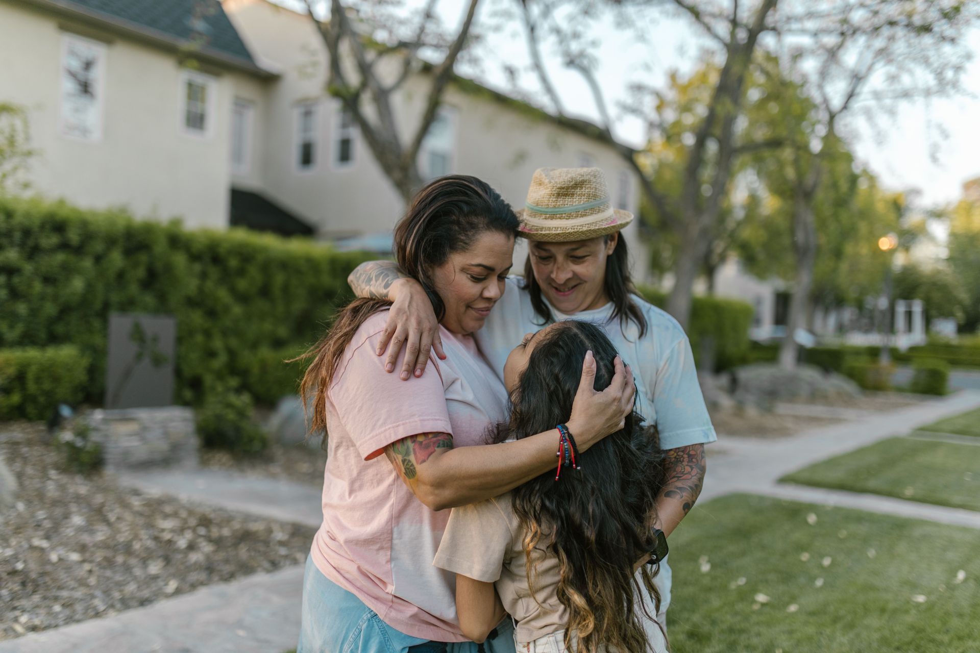 a group of two adults hugging a child outside in front of a home