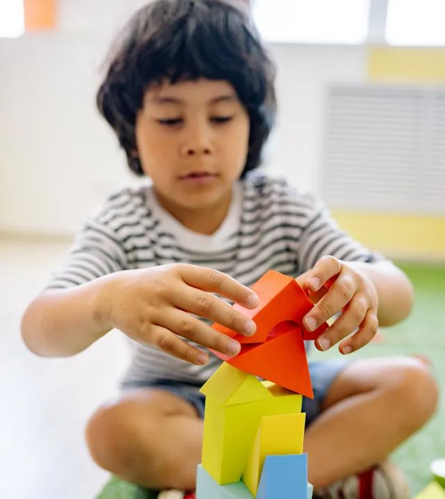 Child stacking colorful blocks on a green mat indoors