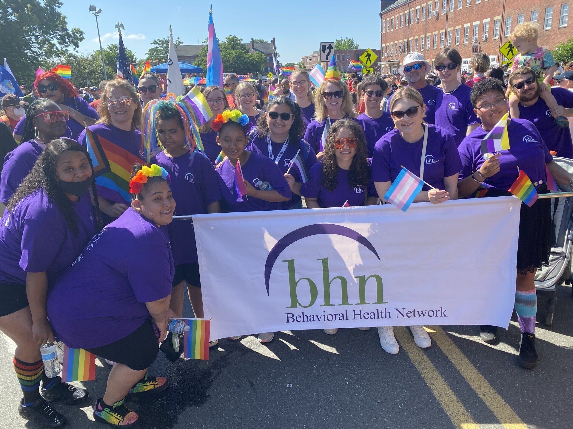 Pride parade group in purple shirts holding a BHN banner on a sunny street