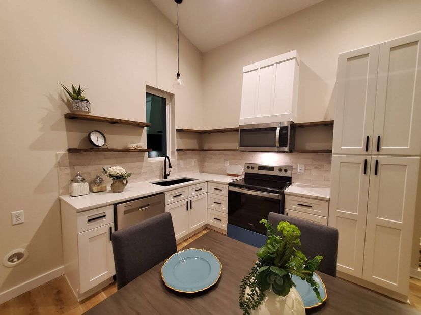 Modern kitchen with white cabinets, black appliances, wood counters, and a small dining table with blue plates