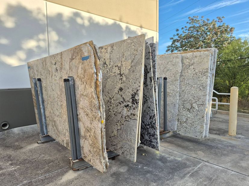 Stacks of granite slabs on metal racks outside a building under a clear sky