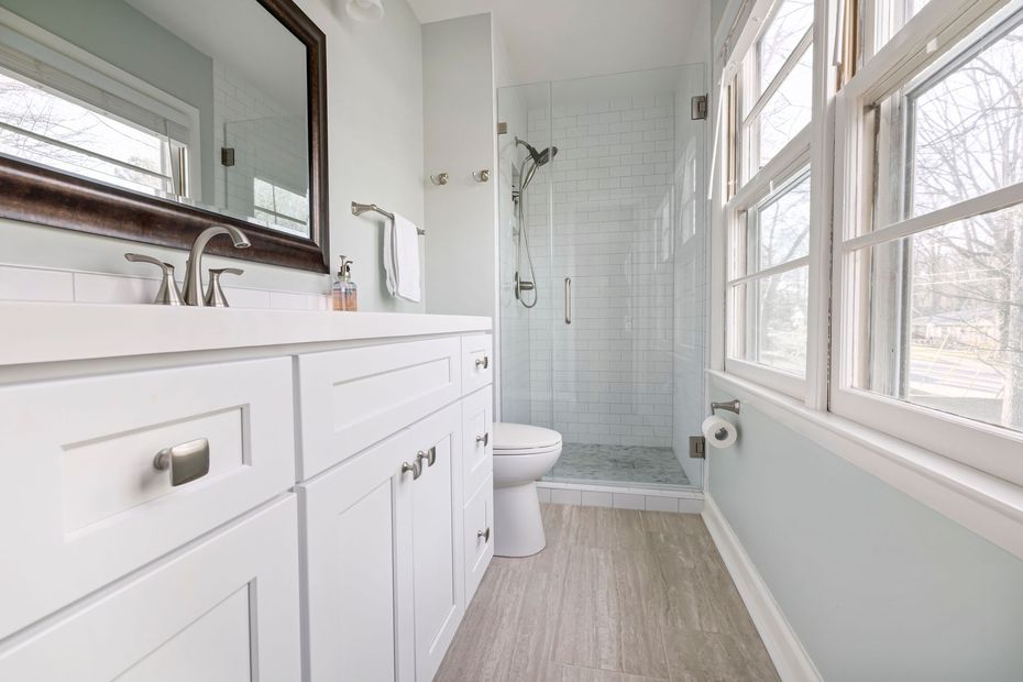 Bright white bathroom with double vanity, large mirror, and tiled walk-in shower by windows