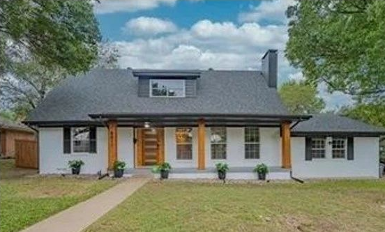 A white house with a black roof and a large porch.