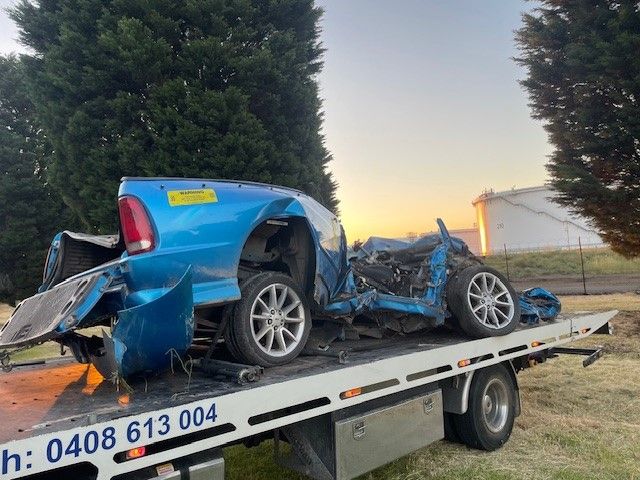 A Man Is Standing Next To A Tow Truck With A Damaged Car On It — Lorne Accident & Assist Towing In Eastern View, VIC