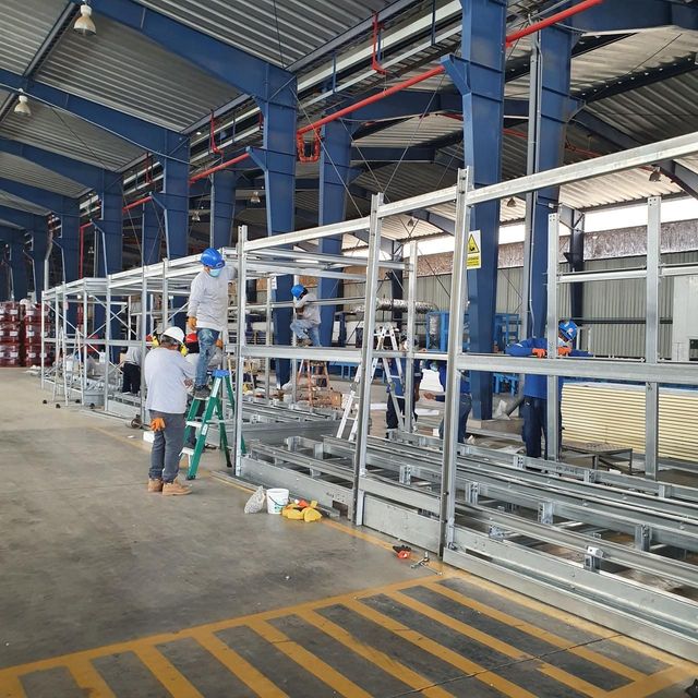 Trabajadores montando una estantería metálica larga en un almacén con columnas azules y suelo de hormigón
