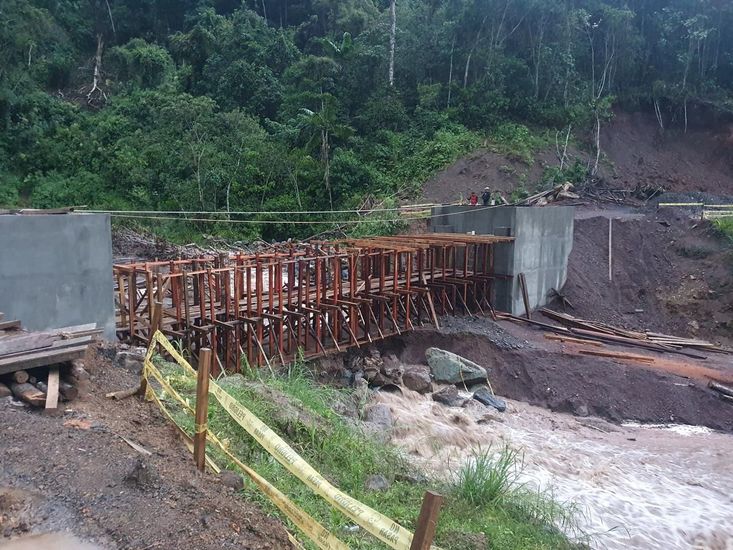 Encofrado de un puente oxidado junto a la orilla embarrada de un río, en una obra rodeada de bosque