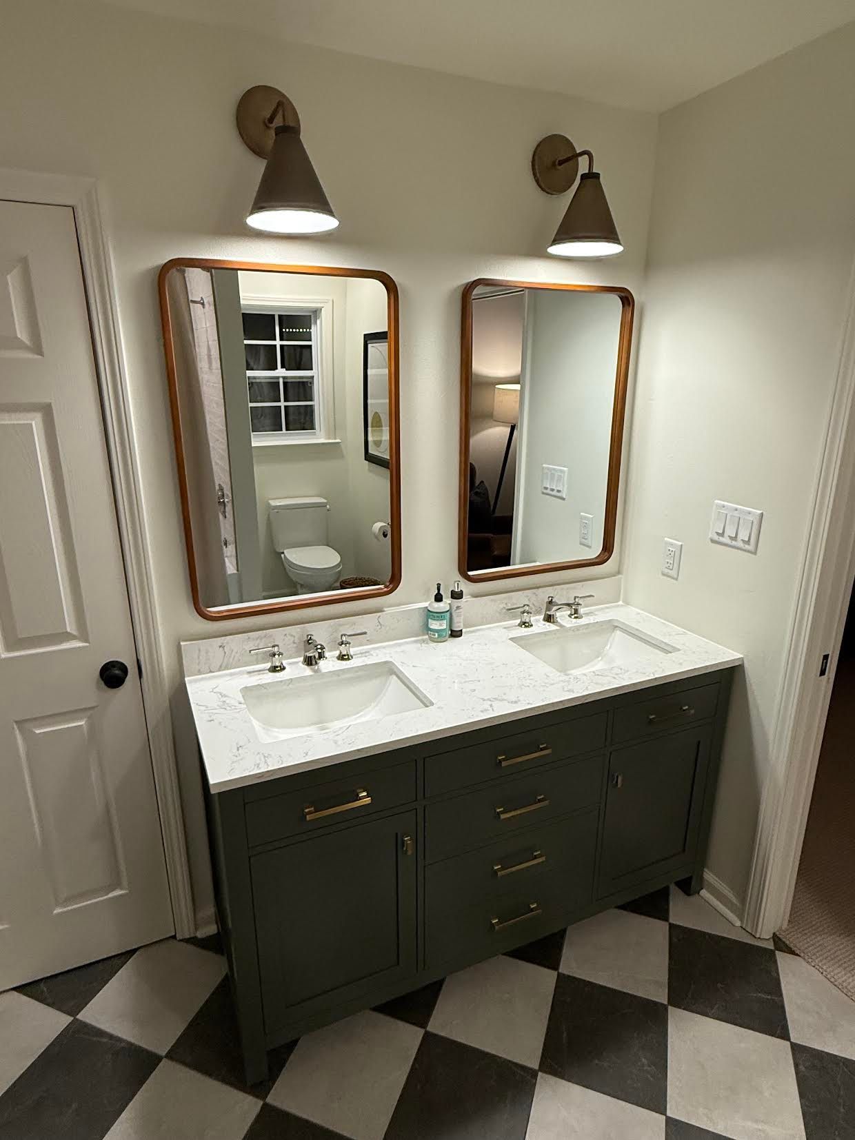 Bathroom vanity with two mirrors, dark cabinets, and black-and-white checkered tile floor.