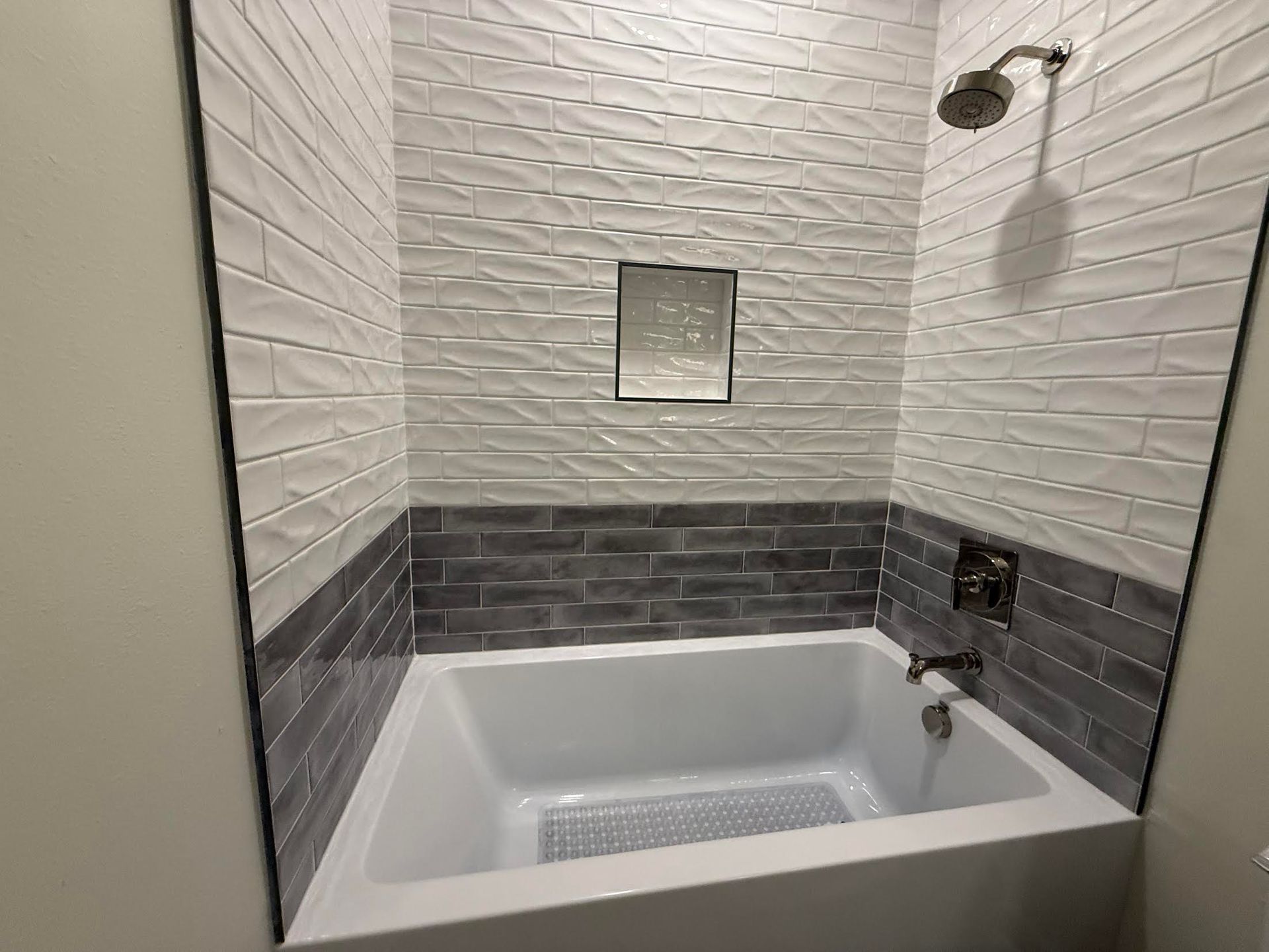 Modern bathroom with a white bathtub, gray tile accent wall, and small wall mirror
