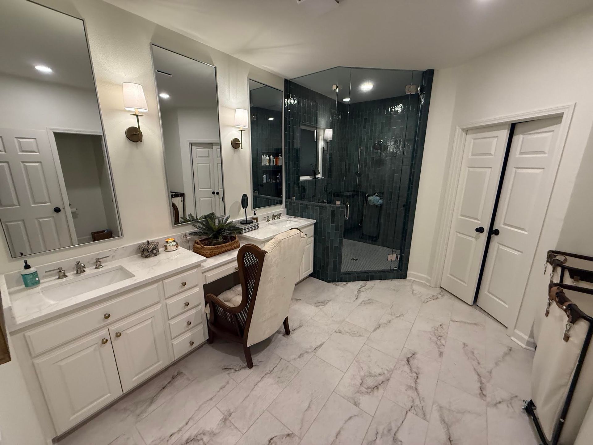 Modern white bathroom with double vanity, large mirrors, and a glass-enclosed dark tiled shower.