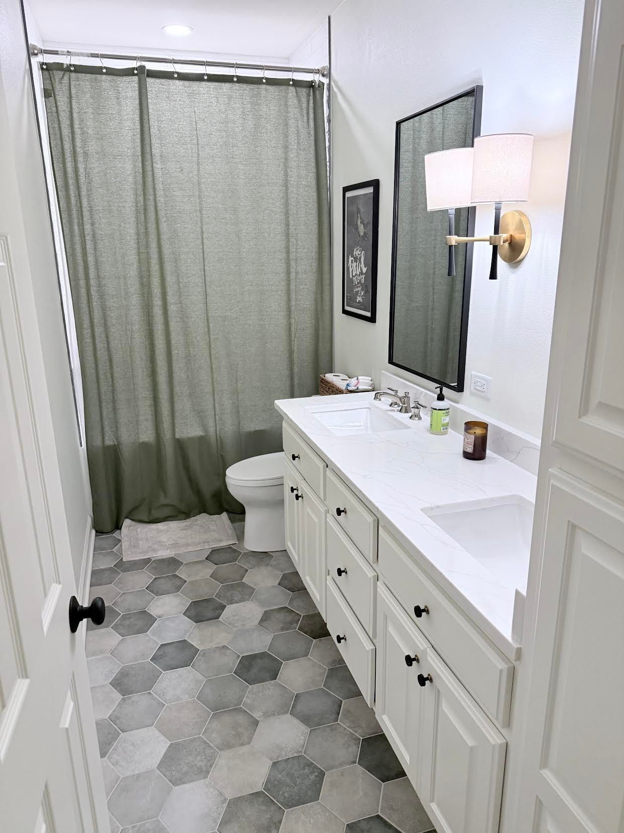 Bright bathroom with white vanity, hex tile floor, shower curtain, mirror, and wall sconce.