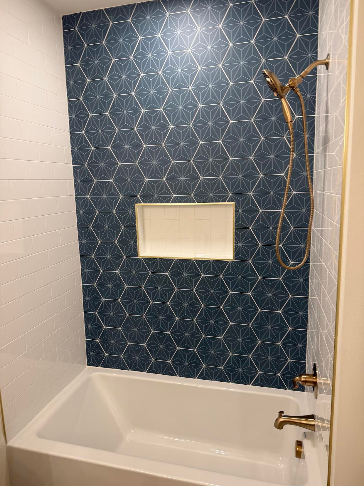 Modern bathtub and shower with blue patterned tile and brass fixtures
