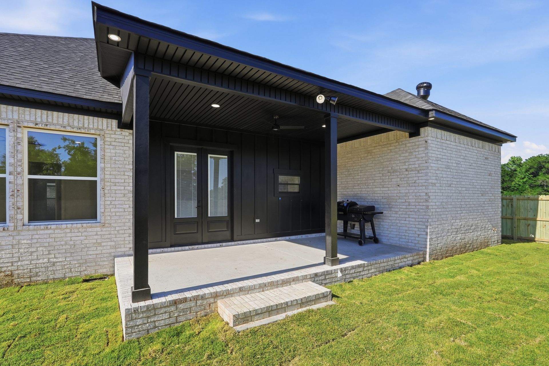 Modern house front porch with black entryway and small steps on a grassy lawn