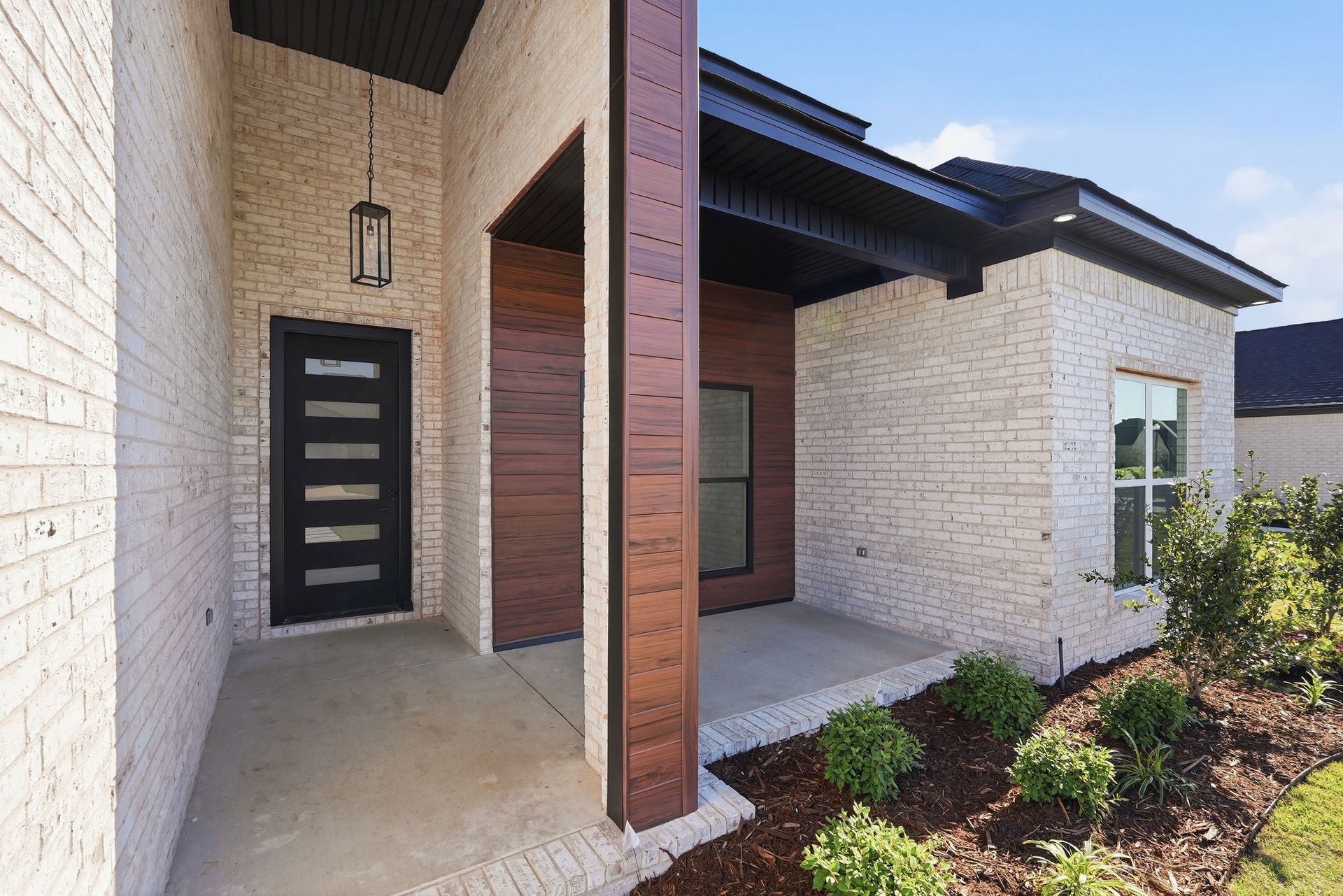 Modern house entrance with brick walls, black front door, and covered porch with landscaping.