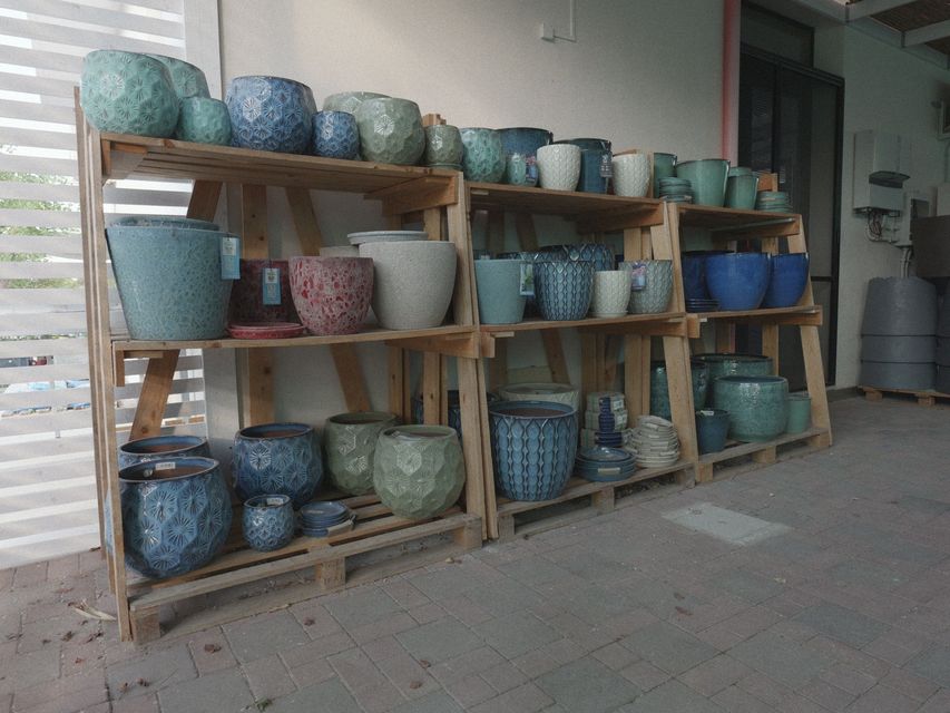 Scaffali con grandi vasi di ceramica blu, verdi e viola esposti lungo un muro all'aperto