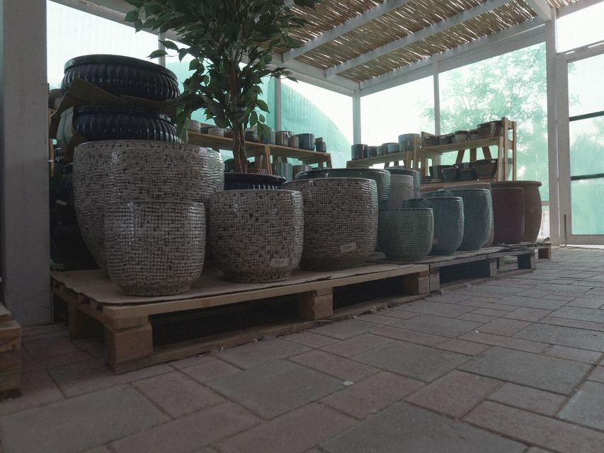 Patio esterno con cesti di vimini impilati e sedie su pallet di legno sotto una tettoia.