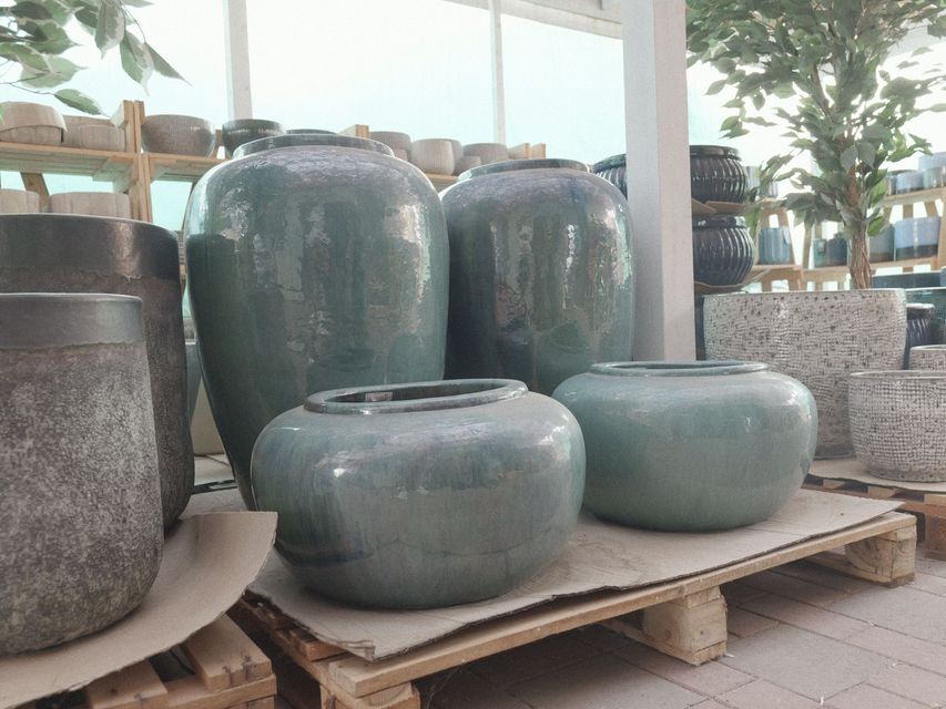 Grandi vasi e ciotole in ceramica verde lucida disposti su pallet di legno all'aperto.
