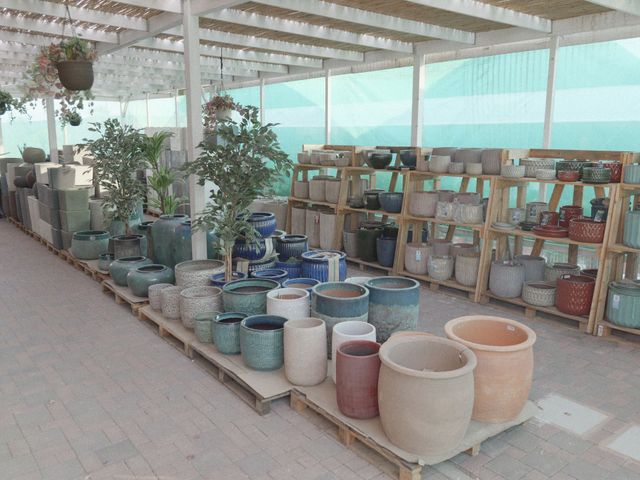 Esposizione di ceramiche all'aperto con file di fioriere e vasi in ceramica su scaffali e a terra sotto una tettoia.