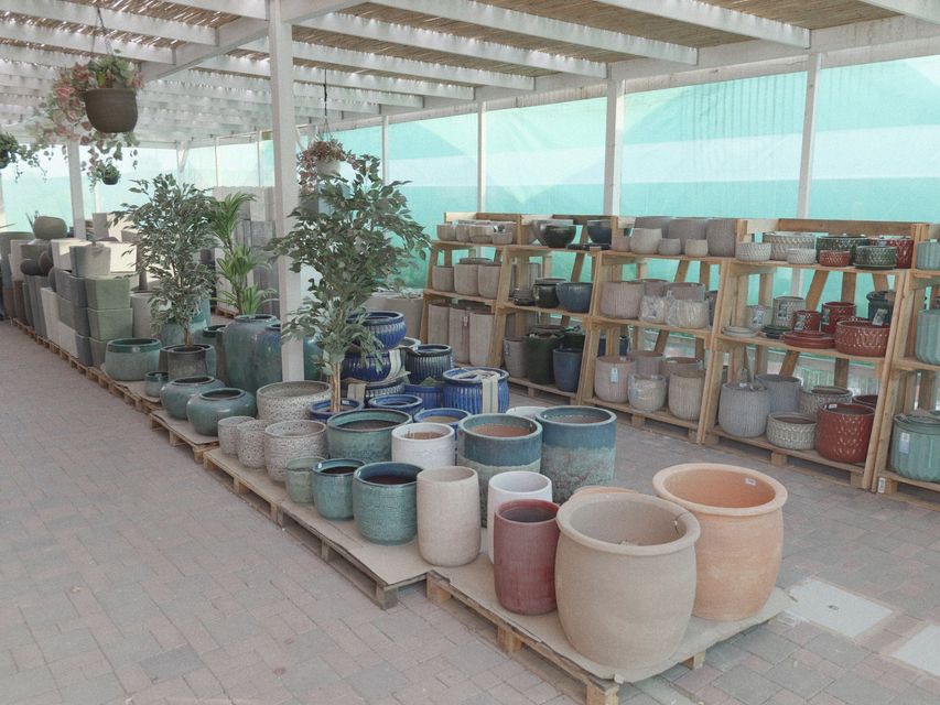 Esposizione di ceramiche al riparo dalle intemperie, con file di fioriere, vasi e fioriere in ceramica su scaffali e tavoli.