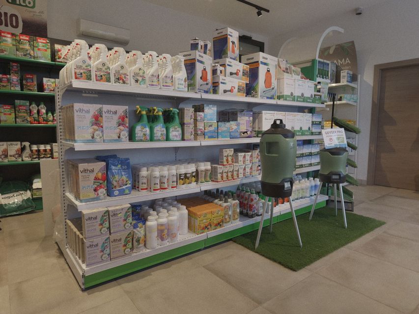 Esposizione di cibo e accessori per animali domestici su scaffali bianchi con tappetini di erba sintetica verde.