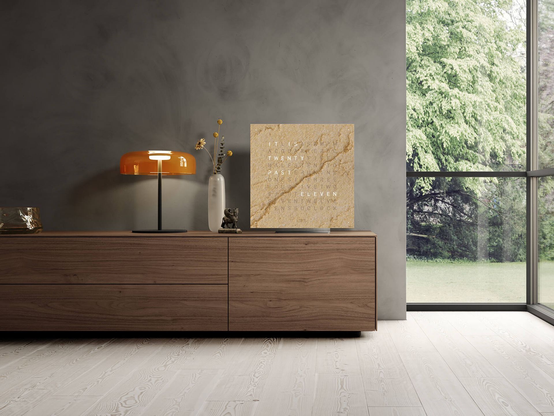 Houten consoletafel met lamp, vaas en klok tegen een donkere muur; groot raam met uitzicht op groen.