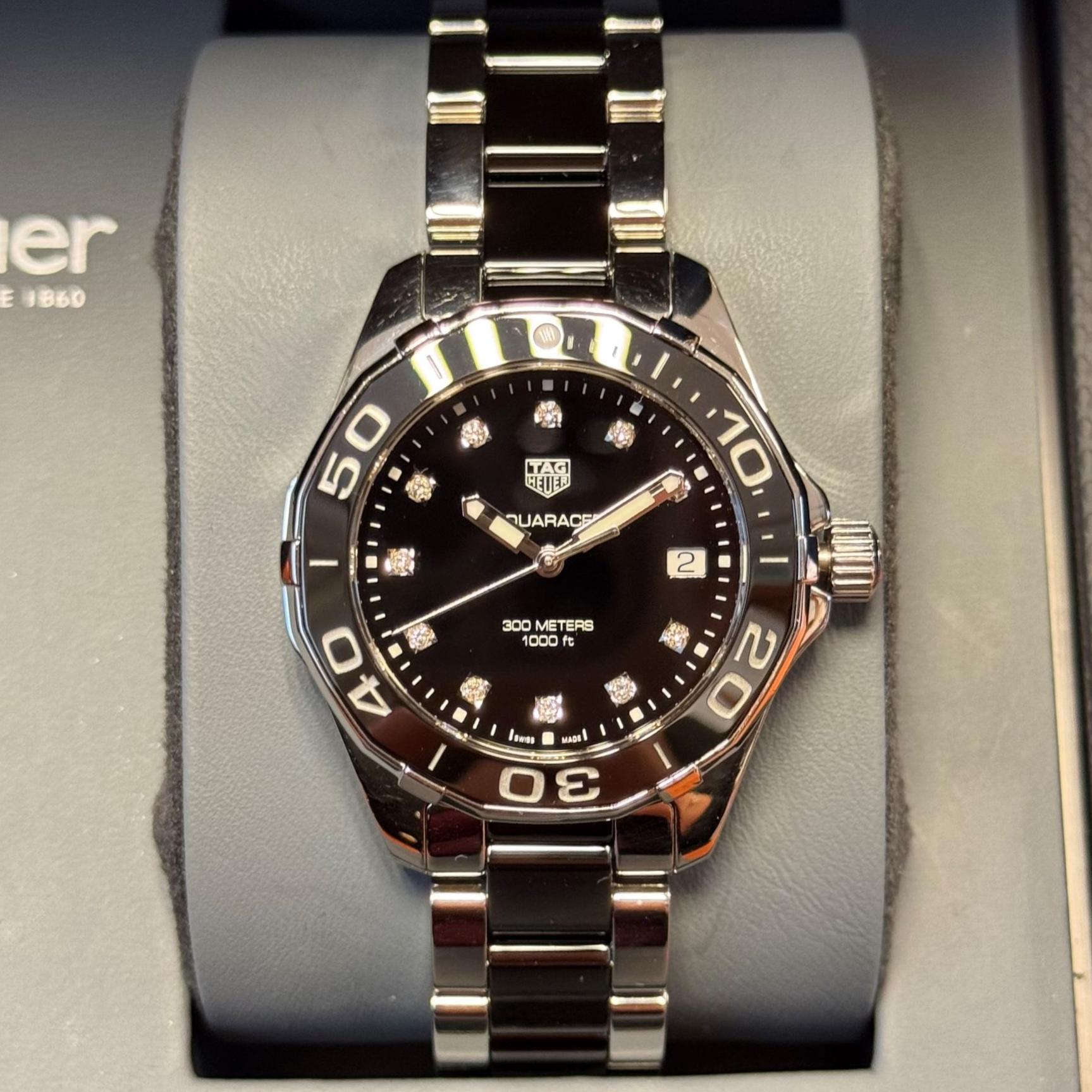 Een zilverkleurig en zwart Tag Heuer Aquaracer horloge met een zwarte wijzerplaat en diamanten uurmarkeringen.