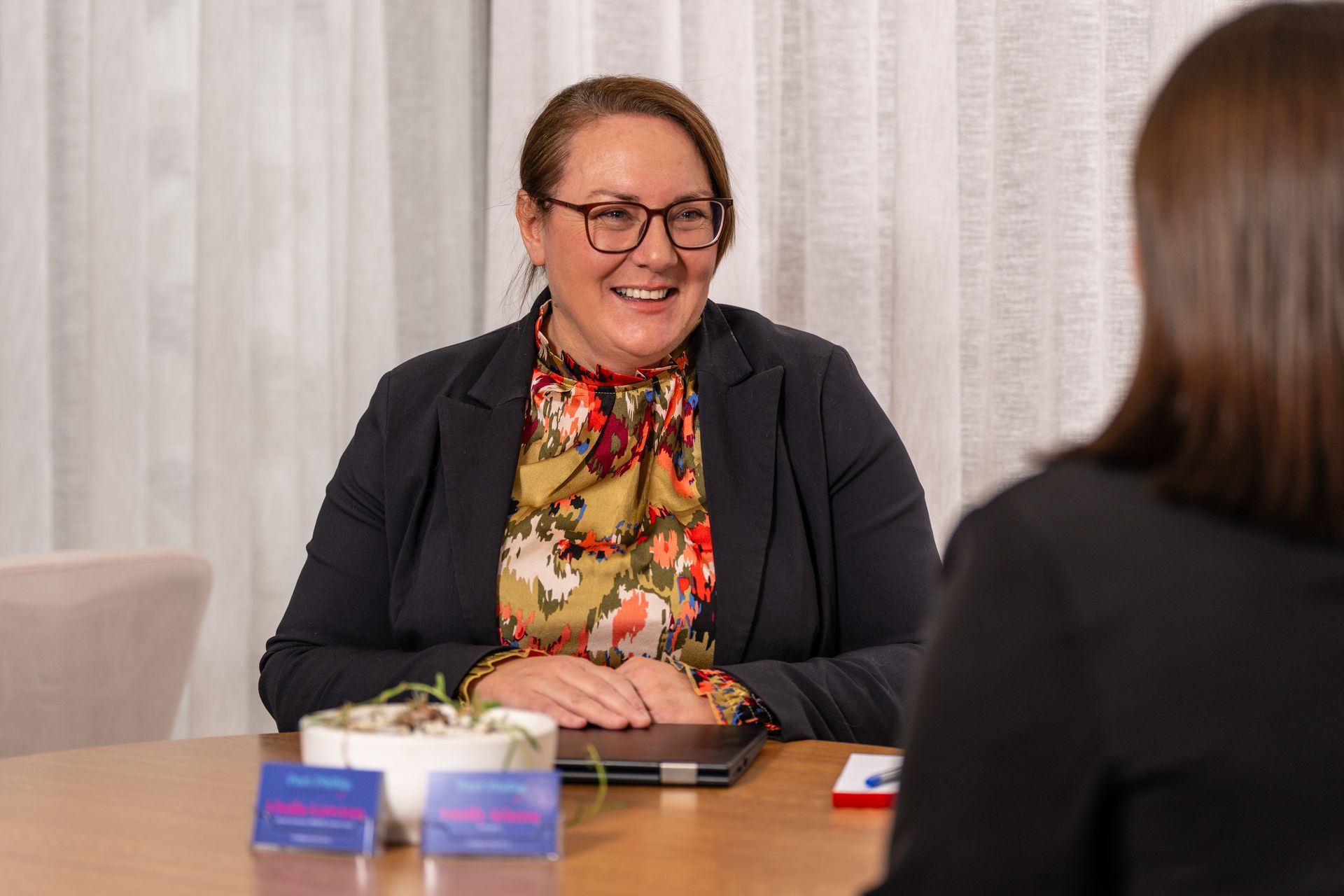Two people seated at a table in conversation, with one smiling and a small tissue box and phone on the table.