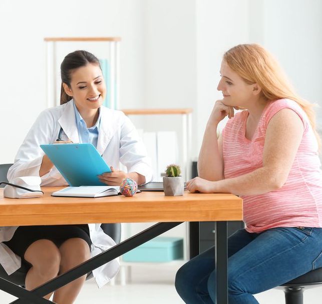 A pregnant woman is sitting at a table talking to a doctor.