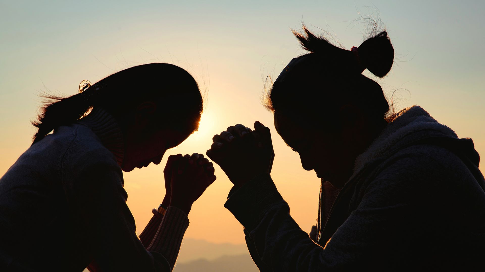 Two silhouetted people clasp hands against a warm sunset sky.