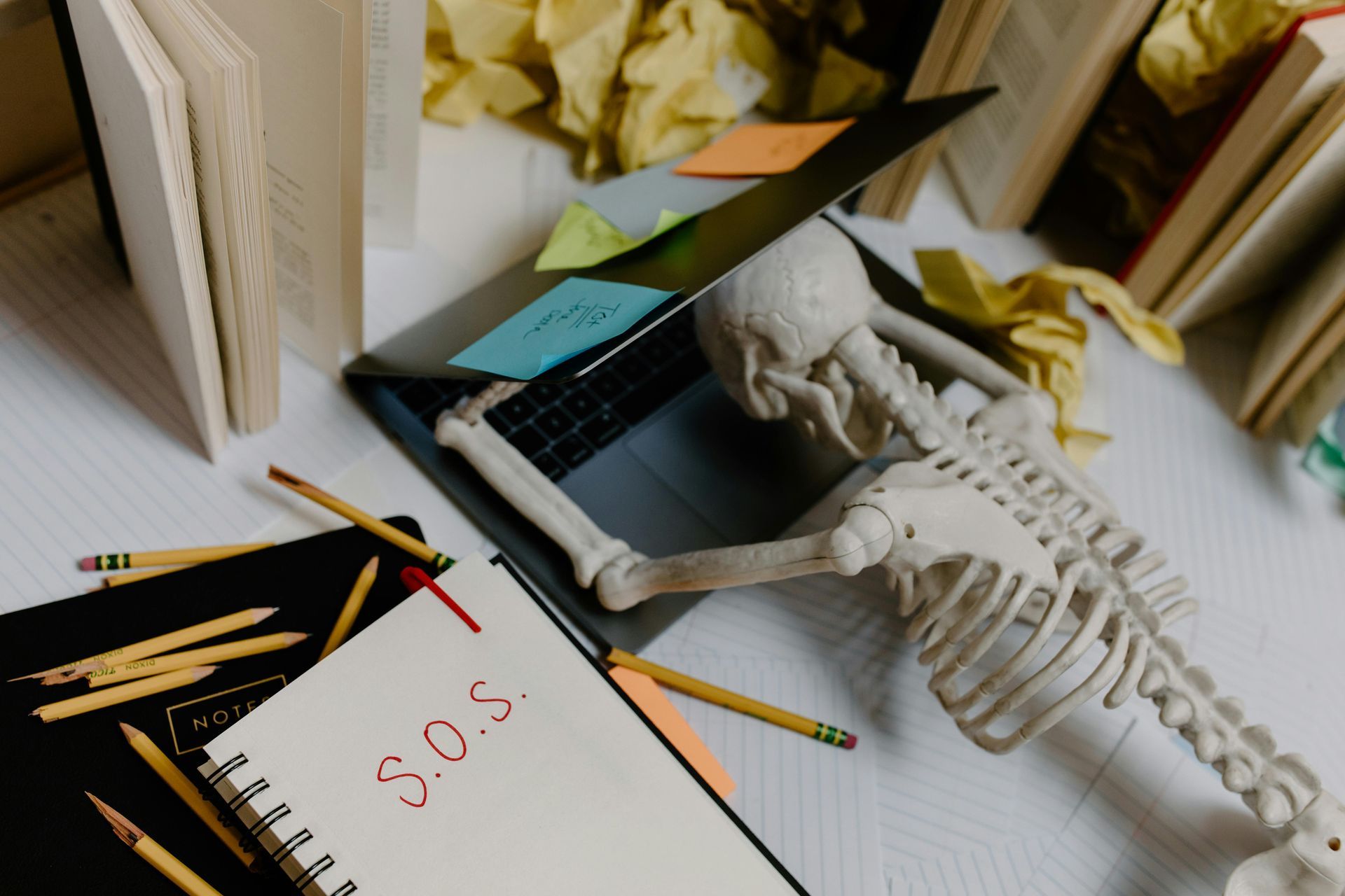 Person skeleton in open book amid notebooks, pencils, and papers on a desk