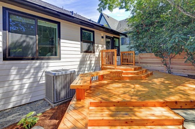 Wooden backyard deck with steps beside a house, surrounded by trees and landscaping.