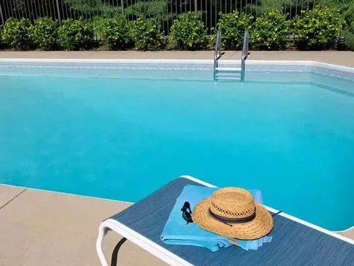 A straw hat is sitting on a lounge chair next to a swimming pool.