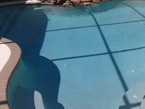 A shadow of a person is reflected in the water of a swimming pool.