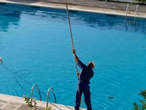 A man is cleaning a swimming pool with a mop.