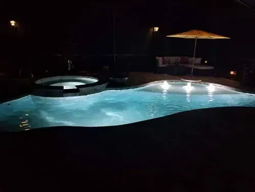 A large swimming pool is lit up at night with an umbrella.
