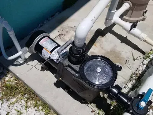 A swimming pool pump is sitting on the ground next to a pool.