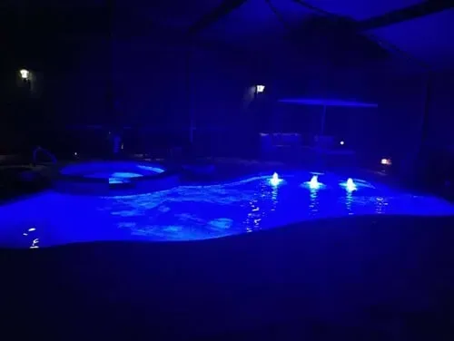 A swimming pool is lit up with blue lights at night